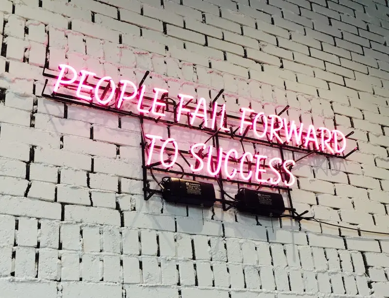 picture of a wall with a neon sign saying -people fail forward to success-